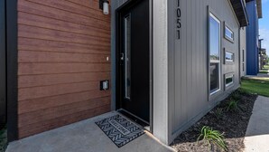 A modern building with a wooden siding exterior, a black door, and a welcome mat. - Dog Parks • Museums • Walking and Biking Trails (Centerton)