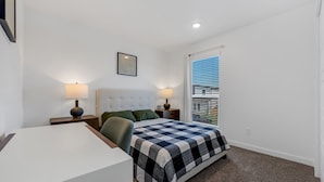 A bedroom with a bed, two bedside tables with lamps, a chair, a desk, and a window with blinds. - Dog Parks • Museums • Walking and Biking Trails (Centerton)