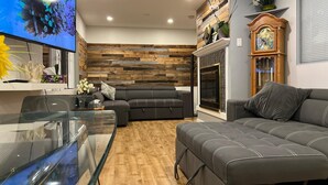 A modern living room with a wooden wall, a fireplace, a television, and a sofa. - Central location, easy dining, Edgemont Village, Rec Centre, & Park Royal Mall.
 (North Vancouver)