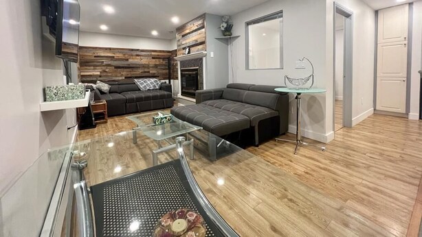 A modern living room with a glass coffee table, a sofa, and a fireplace. - Central location, easy dining, Edgemont Village, Rec Centre, & Park Royal Mall.
 (North Vancouver)