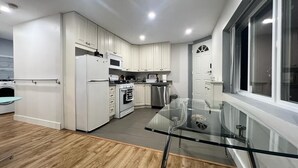 A modern kitchen with white cabinets, stainless steel appliances, and a glass dining table. - Central location, easy dining, Edgemont Village, Rec Centre, & Park Royal Mall.
 (North Vancouver)