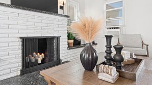 A living room with a white brick fireplace, a black vase with pampas grass, and a wooden coffee table. - Gorgeous Beach Villa -- Ocean Views + Sleeps 12! (San Diego)
