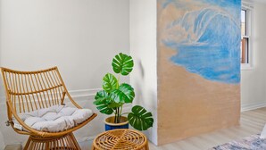A room with a wicker chair, a potted monstera plant, and a beach mural on the wall. - Gorgeous Beach Villa -- Ocean Views + Sleeps 12! (San Diego)