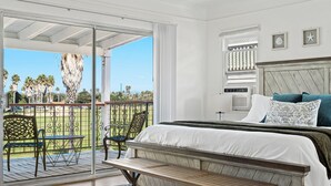 A bedroom with a large bed, a wooden bench, a balcony with chairs, and a view of palm trees. - Gorgeous Beach Villa -- Ocean Views + Sleeps 12! (San Diego)