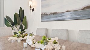 A dining table with a white centerpiece, a painting of a snowy landscape, and a large plant to the left. - Gorgeous Beach Villa -- Ocean Views + Sleeps 12! (San Diego)