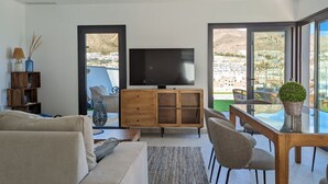 A modern living room with a flat-screen TV, wooden cabinet, and a dining area with chairs and a table. - PANORAMIC pool & mountains house (Finestrat)