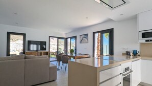 A modern kitchen with a central island, a dining area with chairs, a sofa, and a TV in the living area. - PANORAMIC pool & mountains house (Finestrat)