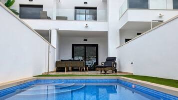 Un moderno edificio residencial con piscina, mobiliario de exterior y balcón.