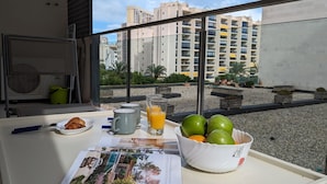 Ein Frühstücksbrett mit Croissants, Saft und Obst auf einem Balkon mit Blick auf eine Stadtlandschaft.