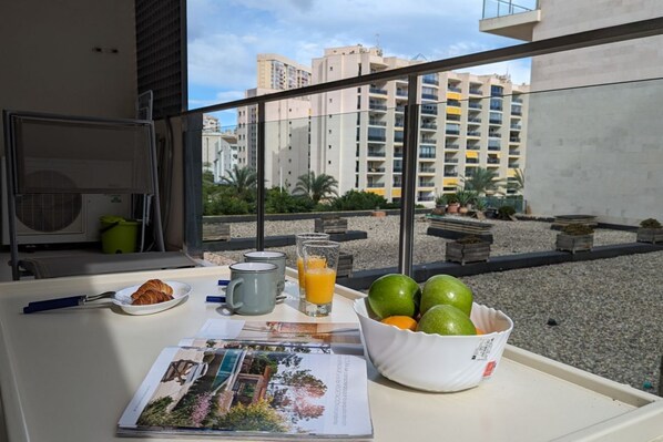 Bandeja de desayuno con croissants, jugo y fruta en un balcón con vista a un paisaje urbano.