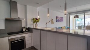 Une cuisine moderne dotée d’un four encastré, d’une hotte en acier inoxydable, de luminaires suspendus et d’un grand îlot central agrémenté d’un vase de fleurs.