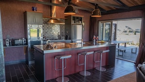 A modern kitchen with a central island, bar stools, and a view of the outdoors. - Holiday Bliss - Tirau, Piarere (Piarere)