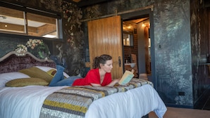 A bed with a patterned bedspread, a wooden headboard, and a person reading a book. - Holiday Bliss - Tirau, Piarere (Piarere)