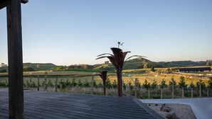 A wooden deck with a view of rolling hills and a distant building. - Holiday Bliss - Tirau, Piarere (Piarere)
