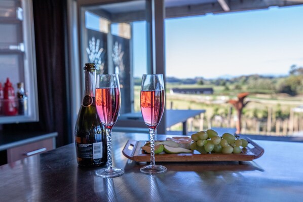 A table with a bottle of wine, two glasses of pink wine, and a wooden board with grapes and sliced apples. - Holiday Bliss - Tirau, Piarere (Piarere)