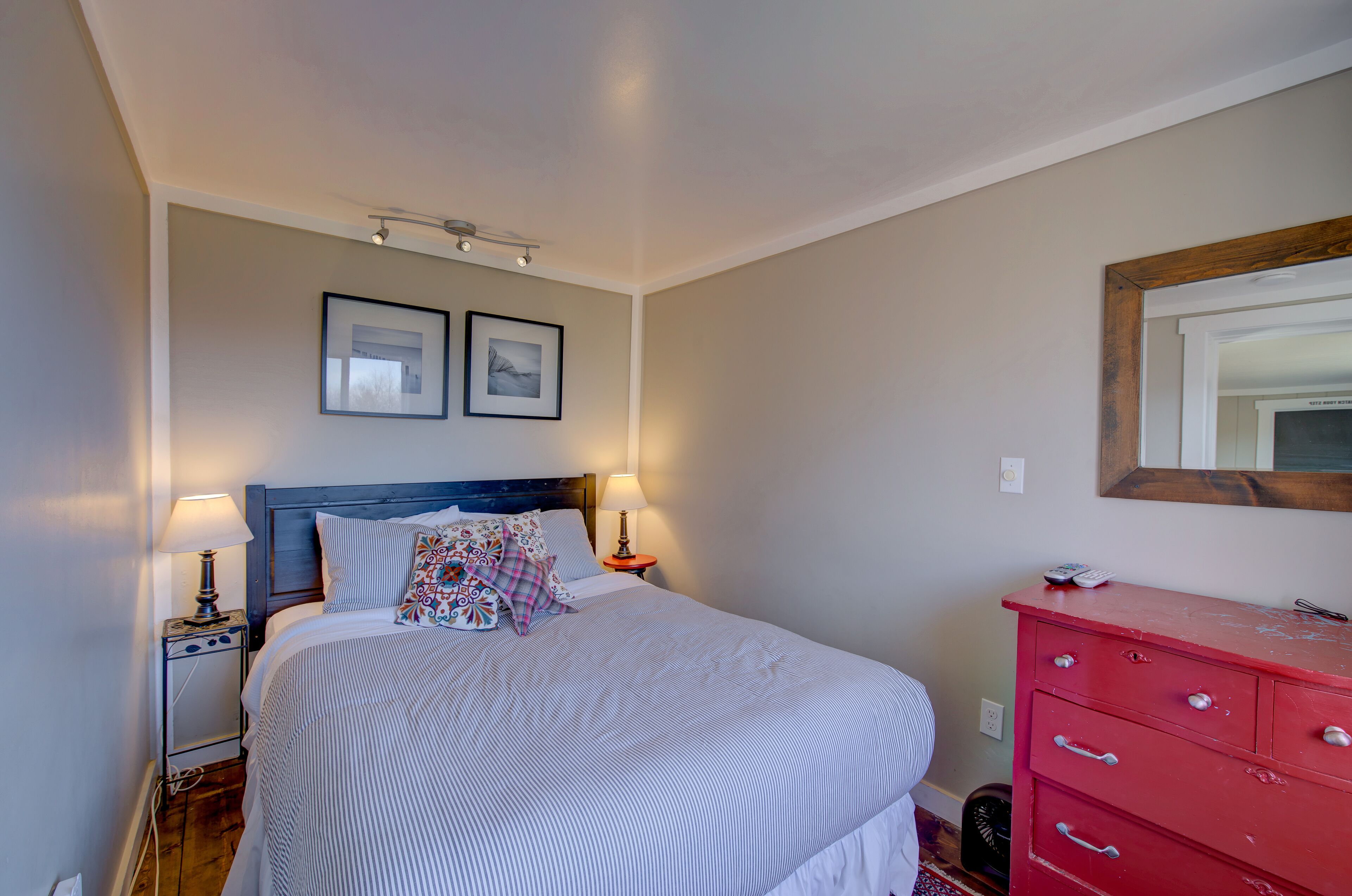 Une chambre à coucher avec un lit, des lampes de chevet, une commode et deux tableaux encadrés au mur.