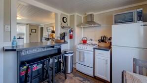 A compact kitchen with a gas stove, microwave, and refrigerator. There are stools at the counter and a trash can. - The Akari Bungalow #5 (Long Beach)
