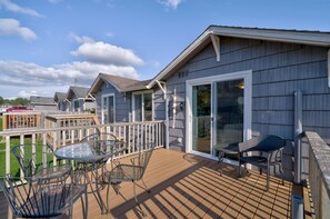 Una terraza con mobiliario exterior, una puerta de vidrio que da a un porche cubierto y vistas a casas vecinas.