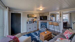 A cozy living room with a fireplace, a television, and a kitchen area visible through an open door. - The Akari Bungalow #5 (Long Beach)