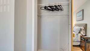Un armari amb porta corredissa que té una paret blanca, un terra de fusta i una barra metàl·lica amb penjadors negres.