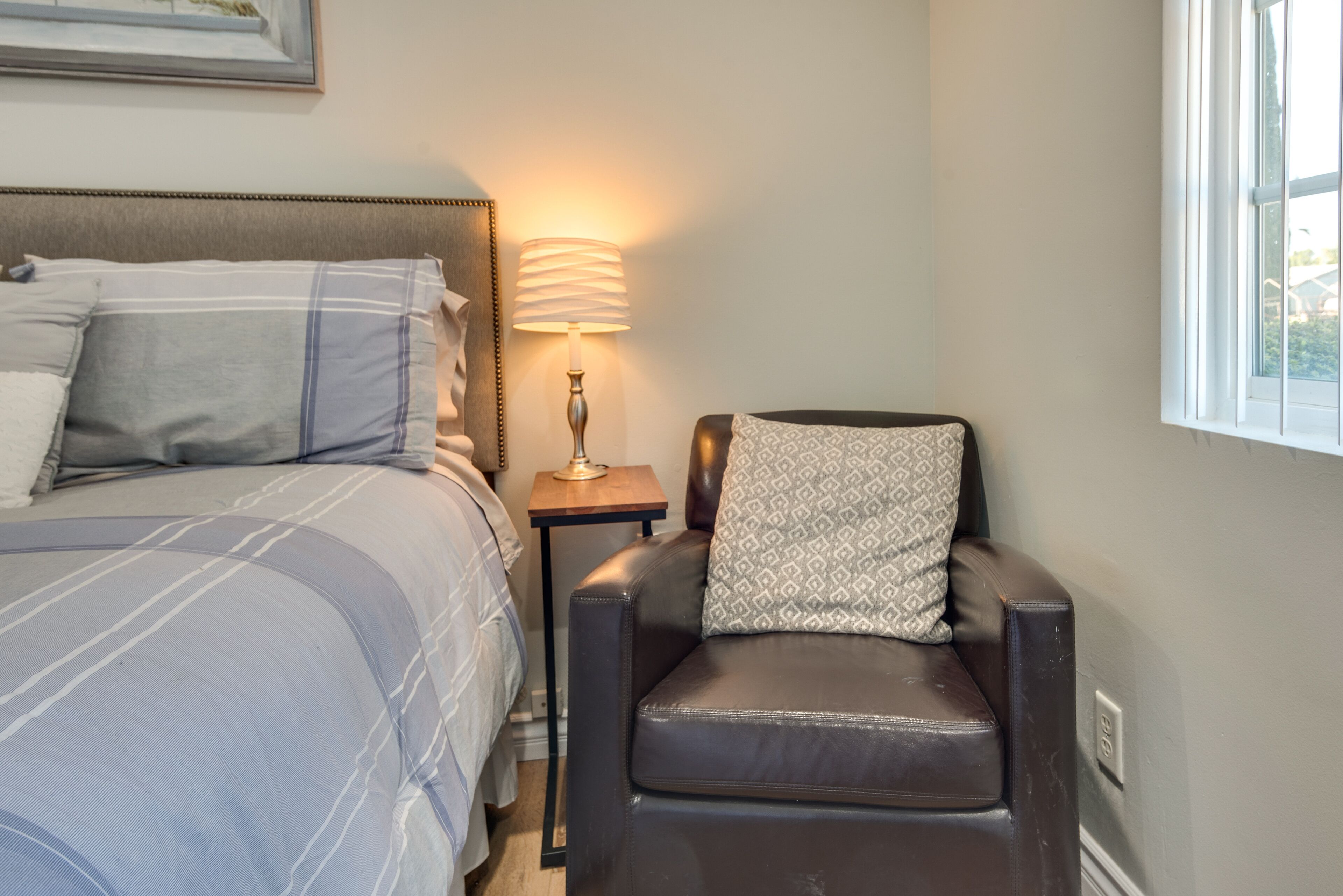 A bedroom with a bed, a chair, a nightstand, and a lamp.