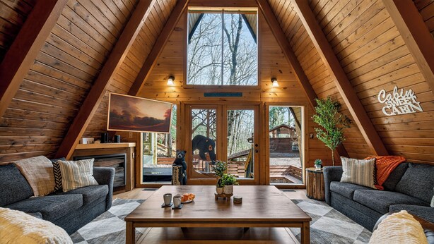 A cozy cabin interior with a wooden ceiling, a central table, two sofas, and a fireplace.