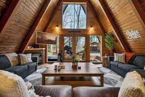 Een gezellig chaletinterieur met een houten plafond, een centrale tafel, twee banken en een open haard.