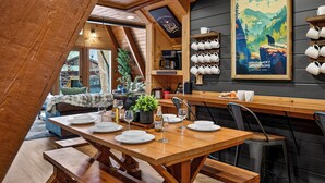 A cozy dining area with a wooden table set for four, benches, and a wall-mounted mug rack.