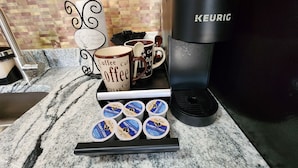 Una encimera de cocina con una cafetera Keurig, tazas de café y recipientes de crumble de arándanos.