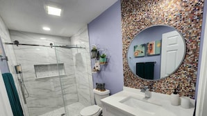 Un baño moderno con cabina de ducha de vidrio, inodoro, lavamanos con espejo y salpicadero de mosaicos.