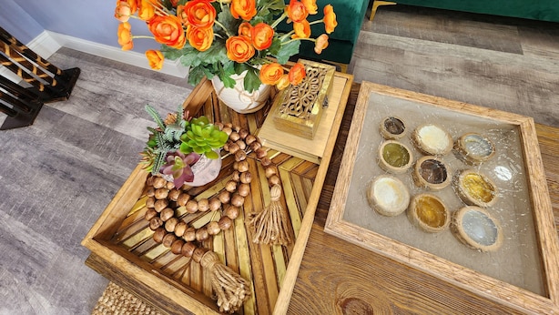 Una bandeja de madera con un jarrón de flores naranjas, una planta suculenta y un adorno de madera.