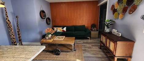 A modern living room with a green sofa, wooden accents, and a decorative wall piece.