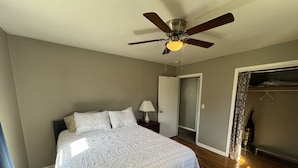 Une chambre à coucher comprenant un lit, un ventilateur de plafond, une table de chevet, une lampe et un placard.
