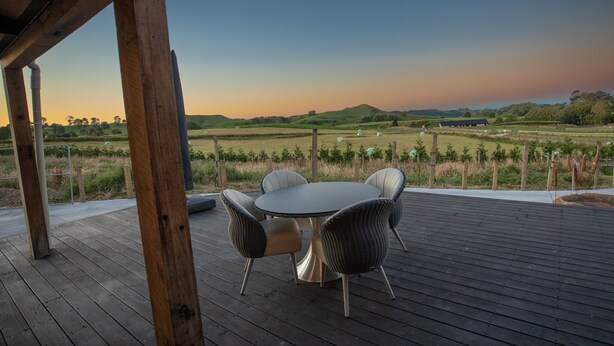 A wooden deck with a round table and chairs, overlooking a vineyard and distant hills.