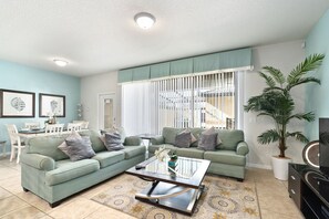 Relax in this stylish living room with a green sofa, glass coffee table, and potted plant.