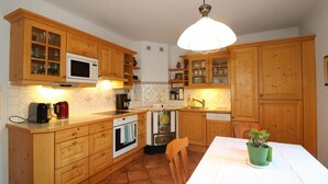 Een keuken met houten kastjes, een magnetron, een fornuis, een spoelbak en een eettafel met een plant.