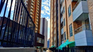 A modern urban street with high-rise buildings, a pedestrian walkway, and a storefront with a green awning.