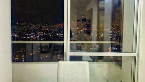 A room with a view of a cityscape at night, a white table with a woven placemat, and a chair.