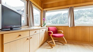 Ein Zimmer mit Holzwänden und Holzdielen, einem Fernseher auf einer Holzkommode, einem roten Sessel und einem Fenster mit Blick auf ein bewaldetes Gebiet.