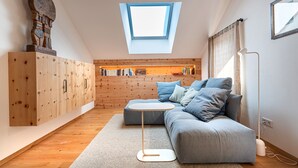 Un dormitorio tipo loft moderno con tragaluces, una estantería empotrada, un sofá gris y una pequeña mesa redonda.