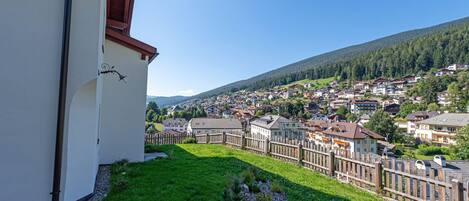 A view of a town with a green lawn and wooden fence in the foreground, and houses in the background.