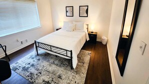 Une chambre à coucher comprenant un lit, un ventilateur de plafond, une table de chevet, un miroir et une fenêtre avec des stores.