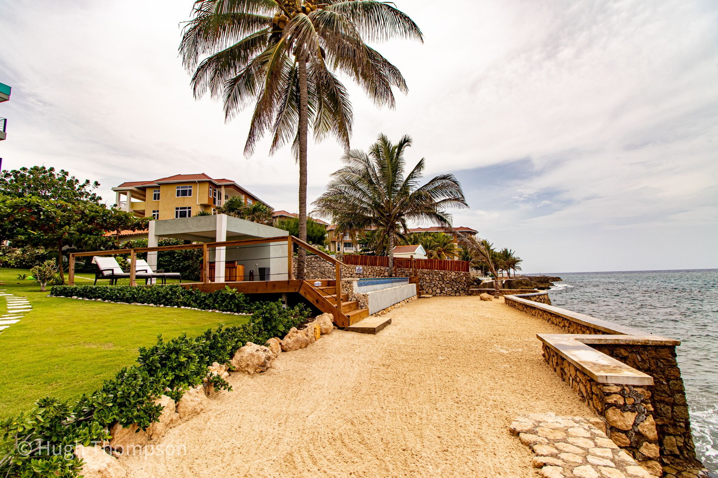 A beachfront property with a sandy beach, palm trees, and a pool area.