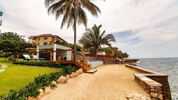 A beachfront property with a sandy beach, palm trees, and a pool area.
