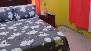 A bedroom with a bed, a nightstand, an air conditioner, and a window with curtains.