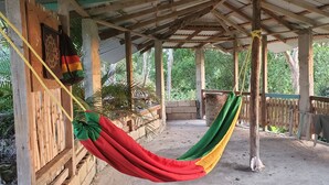 A wooden porch with a hammock, a wooden fence, and a view of greenery.