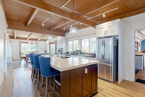 A modern kitchen with a large island, bar stools, and a stainless steel refrigerator.