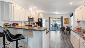 A modern kitchen with white cabinets, a granite countertop, and black bar stools. - Water Slide, Swim Mat, Kayaks! PET FRIENDLY - Retro Weeki Wachee River! (Weeki Wachee)