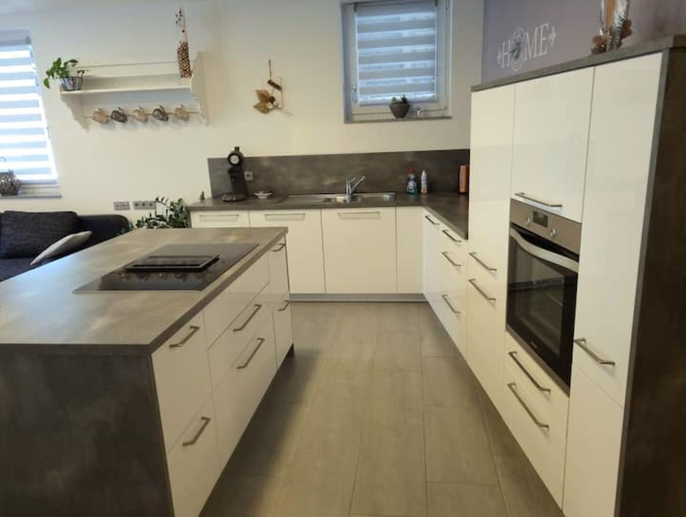 Una cocina moderna con armarios blancos, una isla central, horno empotrado y una ventana con persianas.