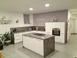 A modern kitchen with a central island, white cabinetry, and a grey backsplash. - Barrierefreie Wohnung mit Terrasse Bodenseenähe (Krauchenwies)